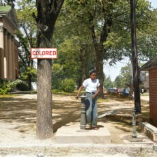 A young African American boy drinks out of a fountain labeled 'Colored'