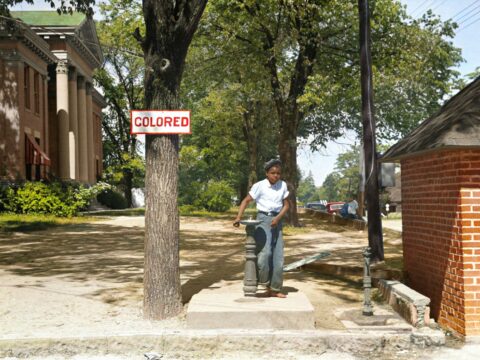 A young African American boy drinks out of a fountain labeled 'Colored'