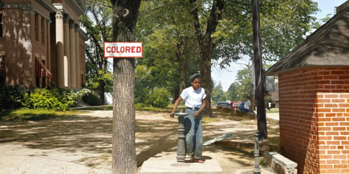 A young African American boy drinks out of a fountain labeled 'Colored'