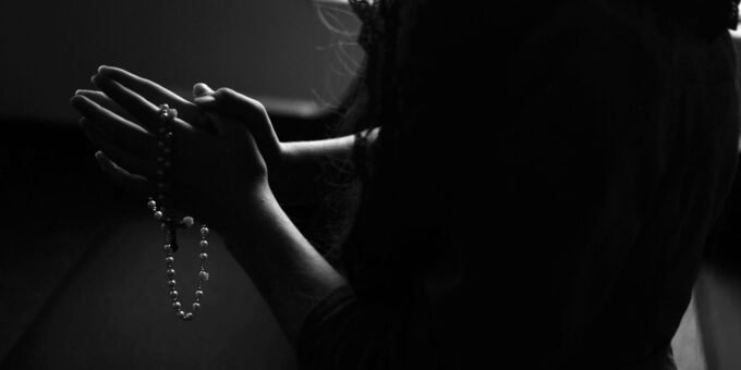 silhouette of woman holding rosary while praying