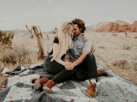 man and woman sitting on blanket while holding each other hands